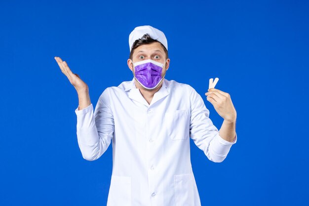 Vue de face du médecin de sexe masculin en costume médical et masque tenant de petits correctifs médicaux sur bleu