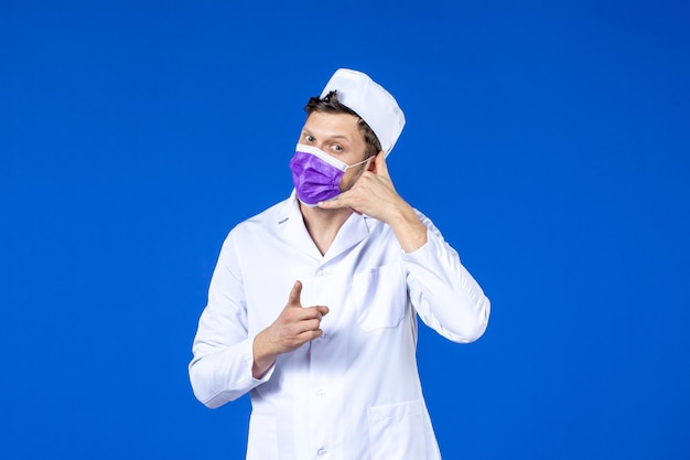 Vue de face du médecin de sexe masculin en costume médical et masque violet sur bleu