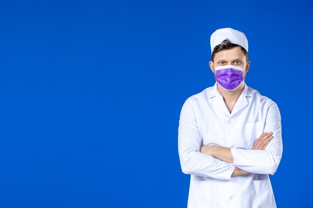 Vue de face du médecin de sexe masculin en costume médical et masque violet sur bleu