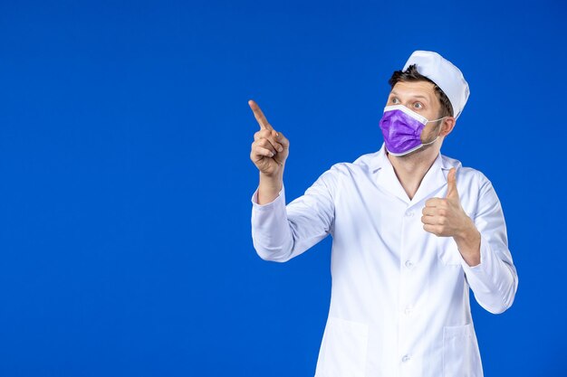 Vue de face du médecin de sexe masculin en costume médical et masque violet sur bleu