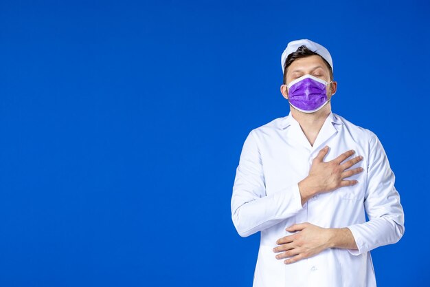 Vue de face du médecin de sexe masculin en costume médical et masque violet sur bleu