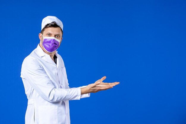 Vue de face du médecin de sexe masculin en costume médical et masque violet sur bleu