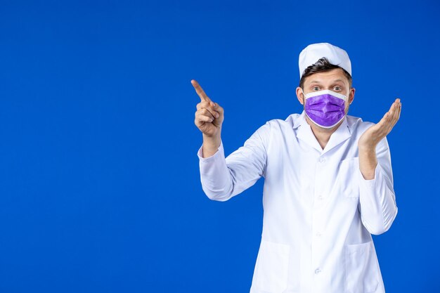 Vue de face du médecin de sexe masculin en costume médical et masque violet sur bleu