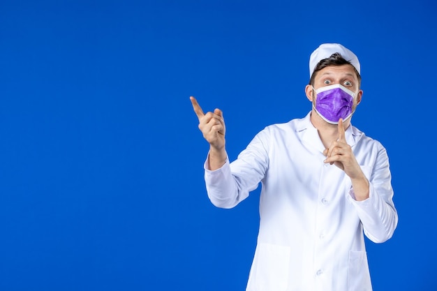 Vue de face du médecin de sexe masculin en costume médical et masque violet sur bleu