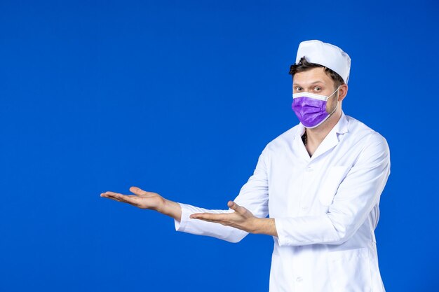 Vue de face du médecin de sexe masculin en costume médical et masque violet sur bleu