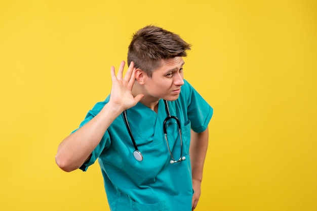 Vue de face du médecin de sexe masculin en costume médical avec stéthoscope sur mur jaune