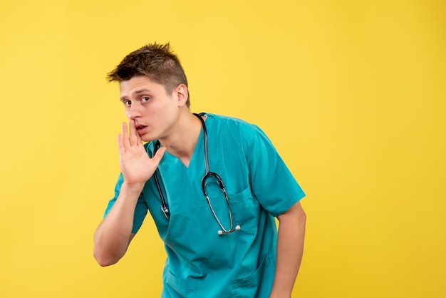 Vue de face du médecin de sexe masculin en costume médical avec stéthoscope sur mur jaune