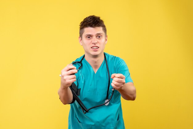 Vue de face du médecin de sexe masculin en costume médical vérifiant sa pression sur le mur jaune