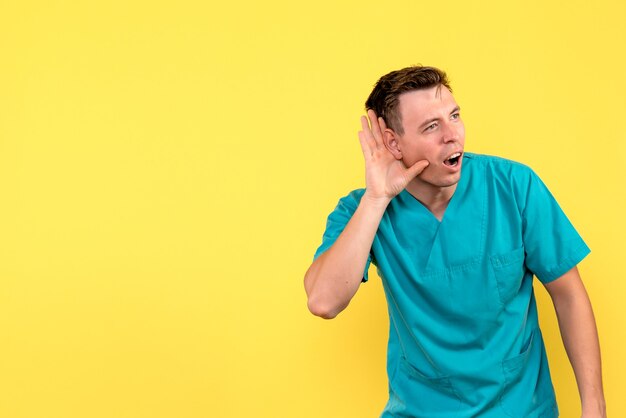 Vue de face du médecin de sexe masculin écoutant attentivement sur le mur jaune