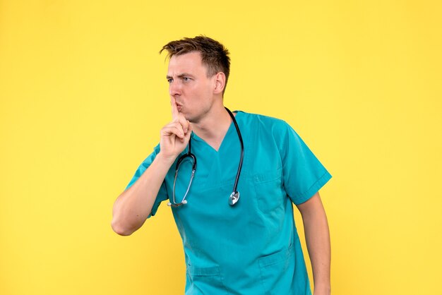 Vue de face du médecin de sexe masculin avec une expression excitée sur le mur jaune