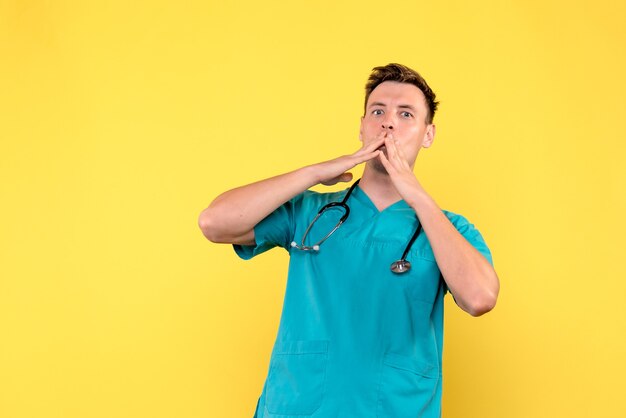 Vue de face du médecin de sexe masculin avec expression nerveuse sur mur jaune