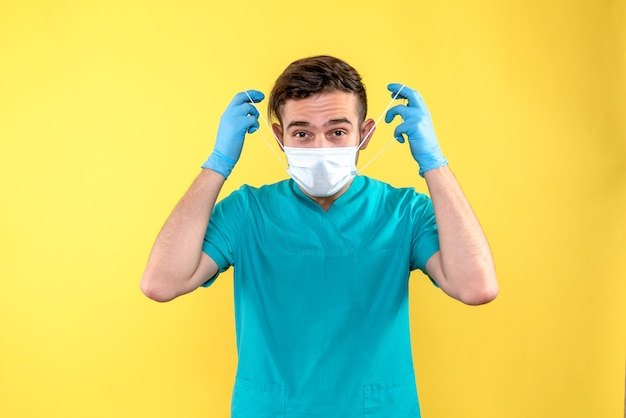 Vue de face du médecin de sexe masculin avec des gants et un masque sur le mur jaune