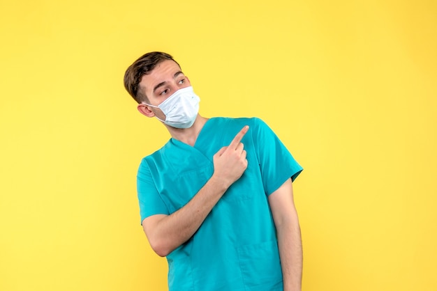 Vue de face du médecin de sexe masculin en masque sur mur jaune