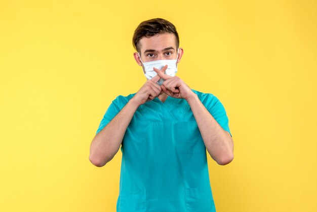 Vue de face du médecin de sexe masculin en masque sur mur jaune