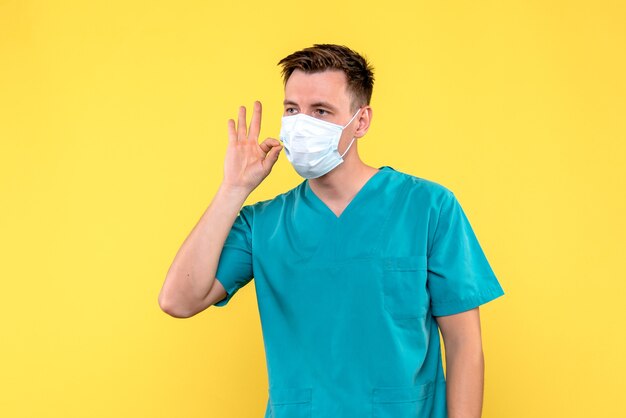 Vue de face du médecin de sexe masculin en masque stérile sur mur jaune