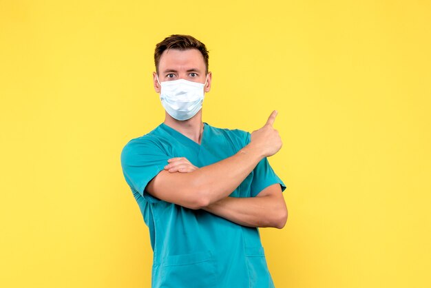 Vue de face du médecin de sexe masculin en masque stérile sur mur jaune