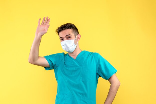 Vue de face du médecin de sexe masculin avec masque stérile sur mur jaune