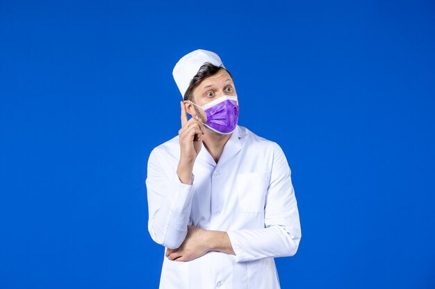 Vue de face du médecin de sexe masculin de la pensée en costume médical et masque violet sur bleu