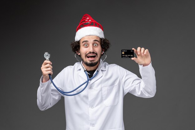 Vue de face du médecin de sexe masculin avec stéthoscope et carte bancaire sur mur sombre