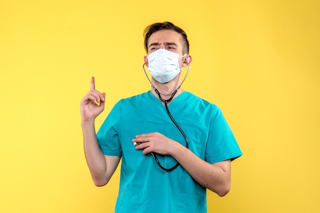 Vue de face du médecin de sexe masculin avec stéthoscope et masque sur mur jaune