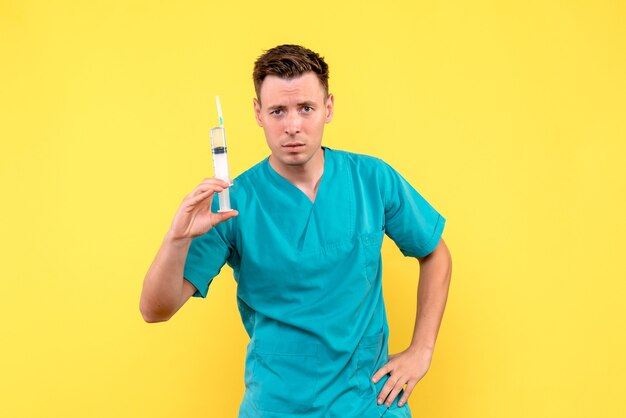Vue de face du médecin de sexe masculin tenant grosse injection sur mur jaune