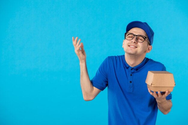 Vue de face du messager masculin en uniforme bleu avec peu de paquet de nourriture sur bleu