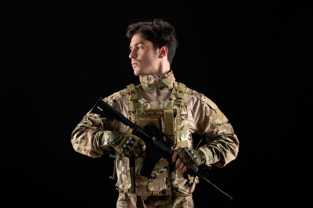 Vue de face du militaire en uniforme avec fusil sur mur noir