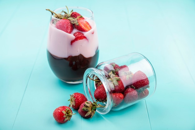 Vue de face du milkshake aux fraises et chocolat sur un verre sur une surface bleue