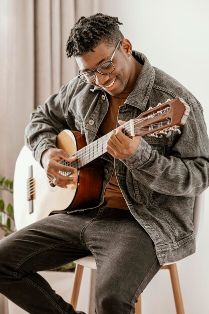 Vue de face du musicien masculin souriant jouant de la guitare à la maison