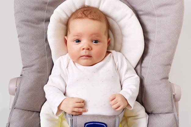 Photo gratuite vue de face du nouveau-né curieux portant un podysuit blanc couché dans une chaise de videur pour enfant