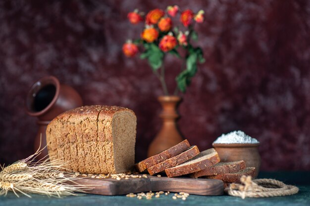 Vue de face du pain noir diététique épis de blé sur une planche à découper en bois bols pot de fleurs sur fond de couleurs mélangées marron bleu