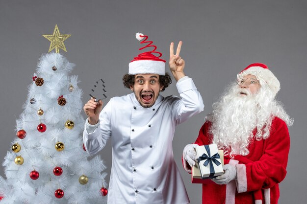 Vue de face du père noël autour de l'arbre de vacances avec un cuisinier masculin