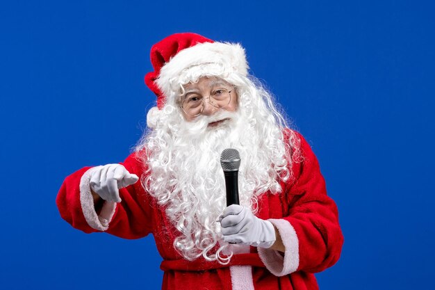 Vue de face du père noël avec un costume rouge et une barbe blanche tenant un micro sur la couleur de noël des vacances de neige bleue