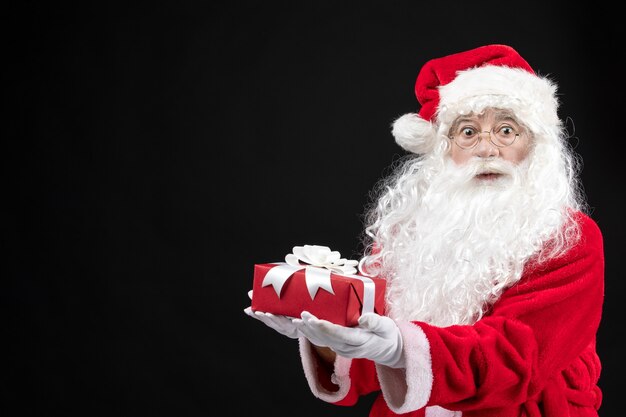 Vue de face du père noël en costume rouge classique tenant un cadeau