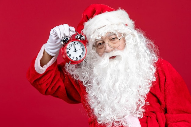 Vue de face du père noël en costume rouge tenant une horloge sur le temps d'émotion des vacances de noël rouge