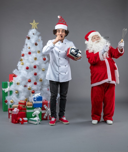 Vue de face du père Noël avec cuisinier et cadeaux de Noël autour sur le mur gris