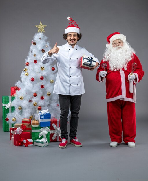 Vue de face du père Noël avec cuisinier et cadeaux de Noël autour sur le mur gris