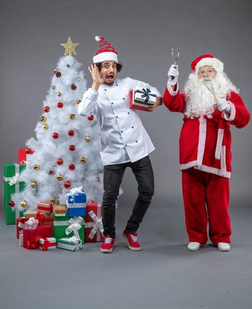 Vue de face du père Noël avec cuisinier et cadeaux de Noël autour sur le mur gris