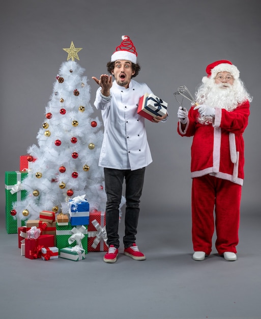 Vue de face du père Noël avec cuisinier et cadeaux de Noël autour sur le mur gris