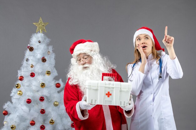 Vue de face du père Noël avec une femme médecin qui lui a donné une trousse de premiers soins sur le mur gris