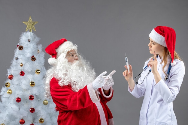 Vue de face du père Noël avec femme médecin qui tient l'injection sur le mur gris