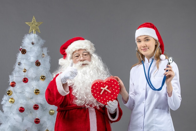 Vue de face du père Noël avec femme médecin tenant présent sur le mur gris