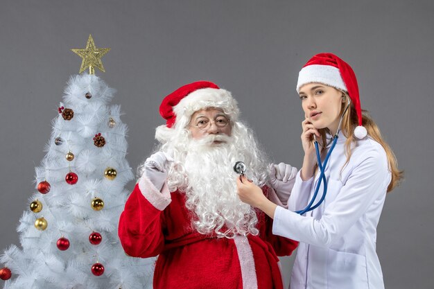 Vue de face du père Noël avec femme médecin tenant présent sur le mur gris