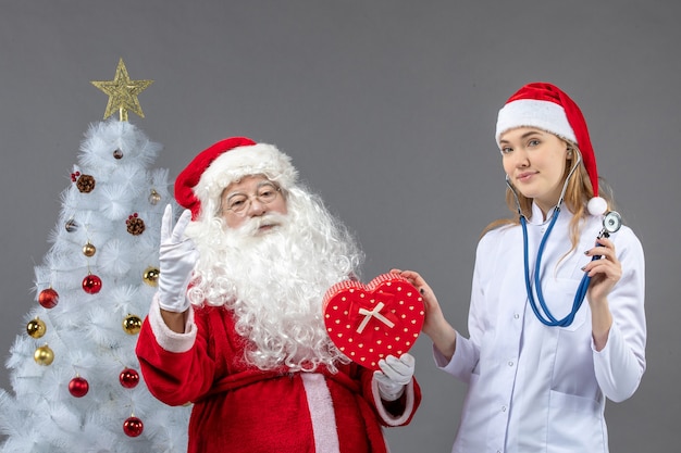 Vue de face du père Noël avec femme médecin tenant présent sur le mur gris