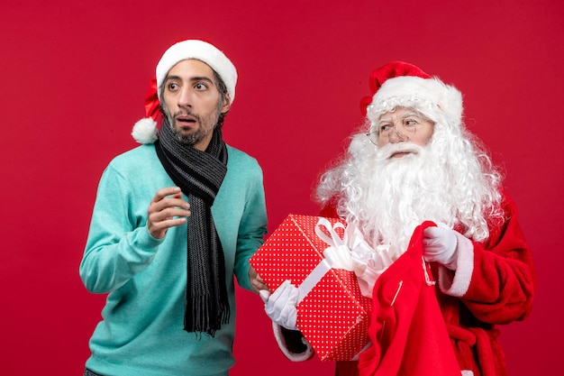 Vue de face du père noël avec un homme sortant un cadeau du sac sur la couleur rouge des vacances d'émotion de noël