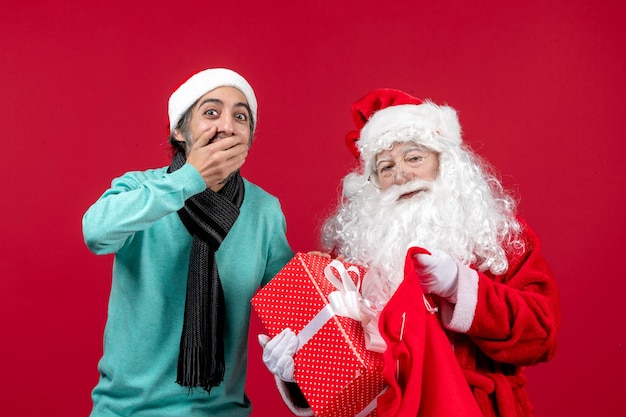 Photo gratuite vue de face du père noël avec un homme sortant un cadeau du sac sur les vacances rouges couleur de l'émotion de noël