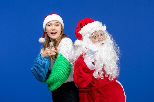 Vue de face du père noël avec une jeune femme juste debout sur le mur bleu