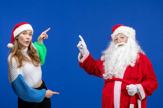 Vue de face du père noël avec une jeune femme juste debout sur le mur bleu