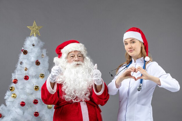 Vue de face du père Noël avec jeune femme médecin sur le mur gris