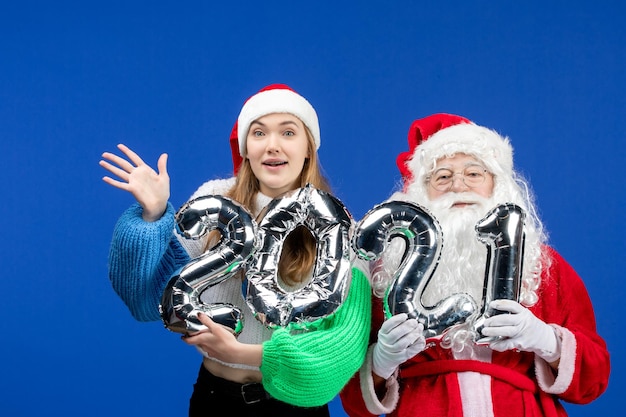 Vue de face du père noël avec une jeune femme tenant une figure sur le mur bleu